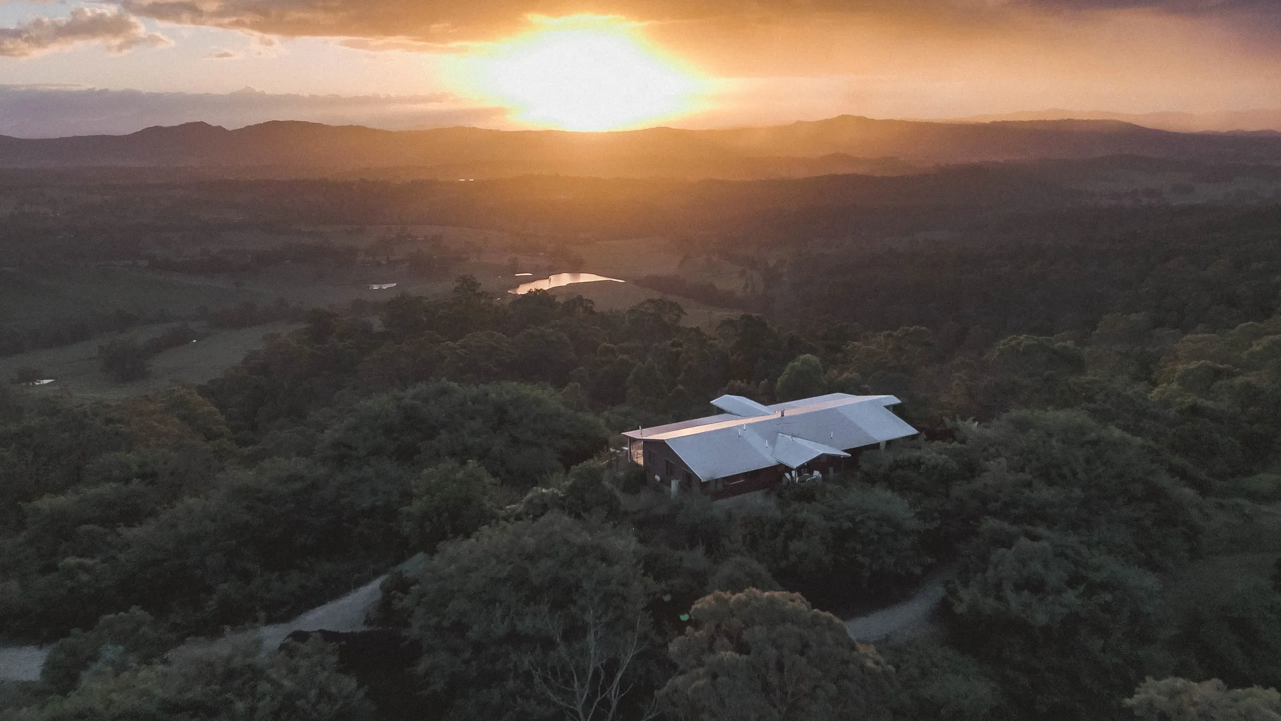 Golden-hour aerial of the guest house on its ridgeline above the Sarabah Valley